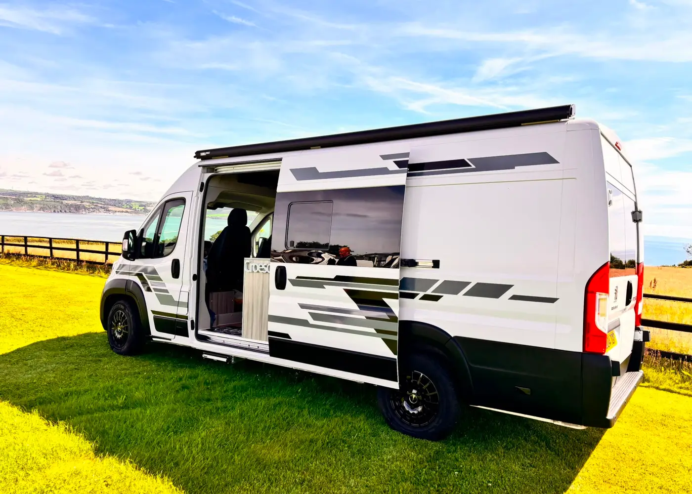 Campervan with open door showing converted interior, parked in front of mountains